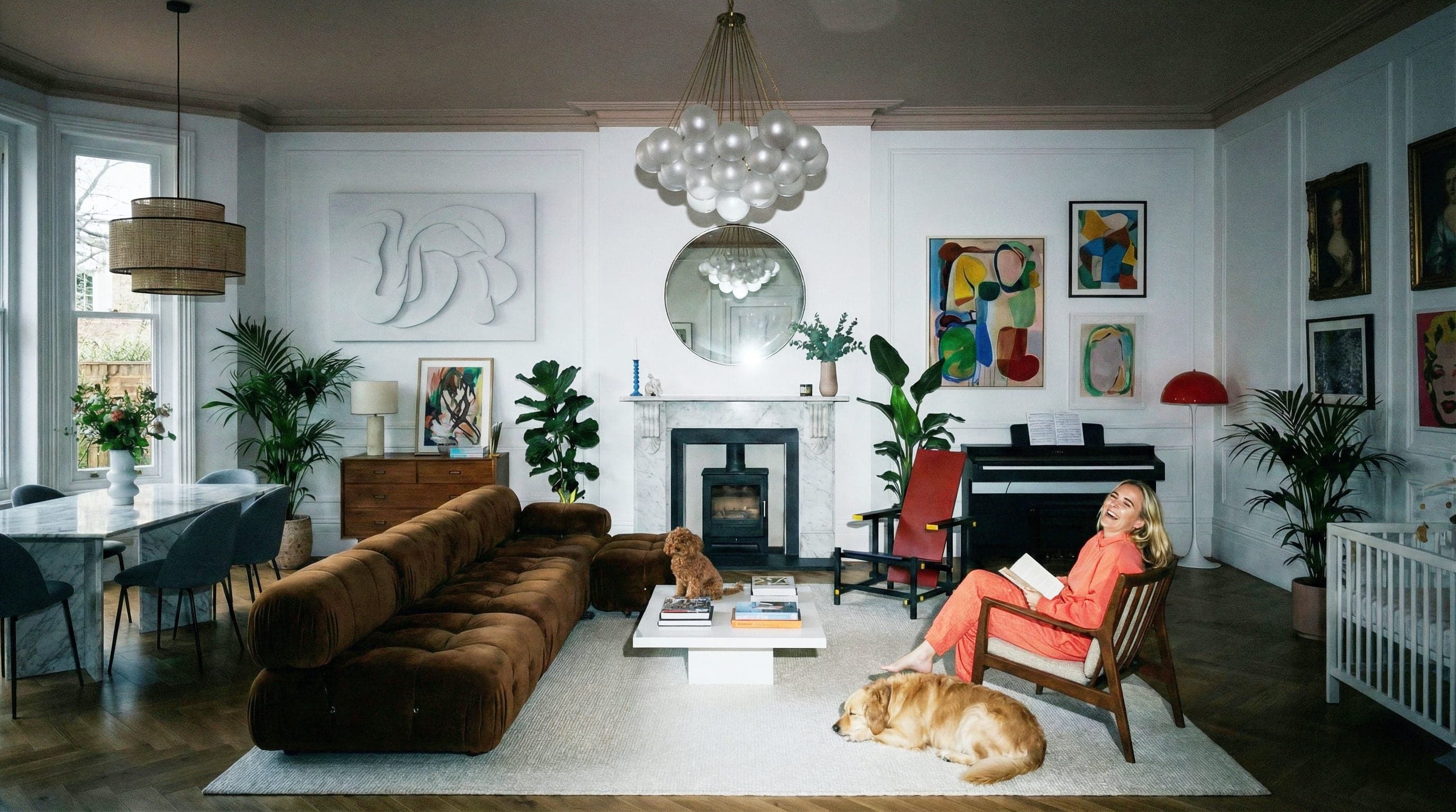 Persoon zit in een fauteuil en leest een boek in een modern ingerichte woonkamer met kunstwerken, piano, open haard en twee honden