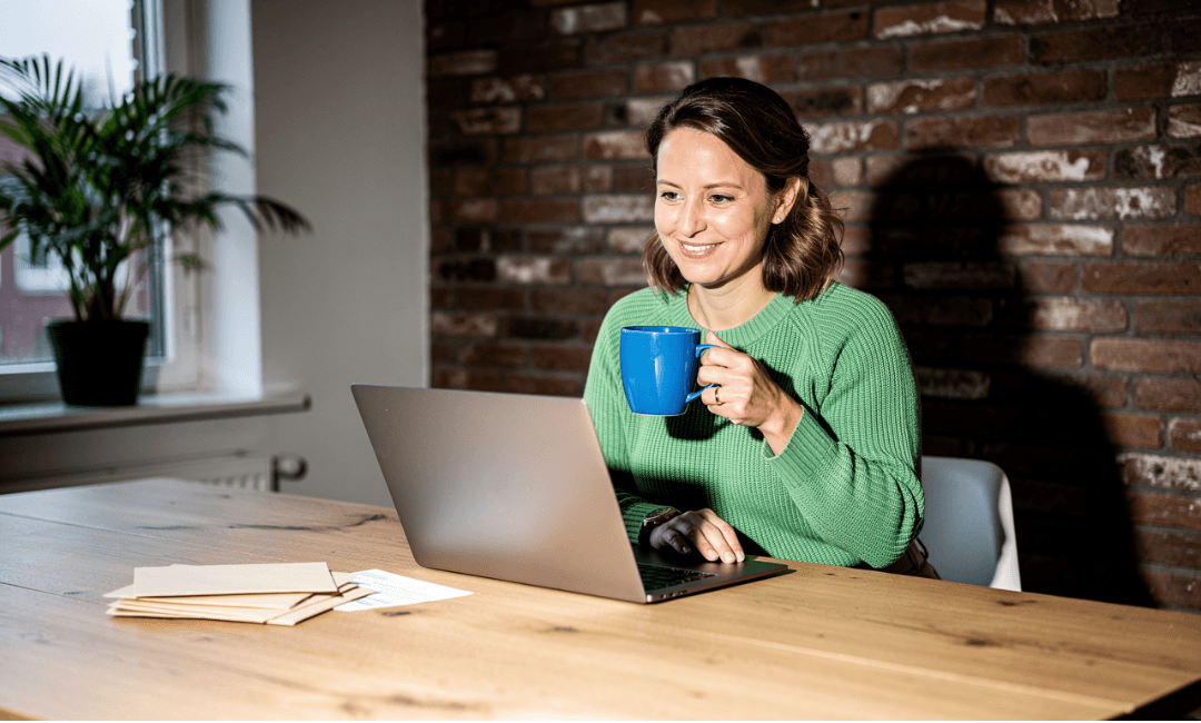 Vrouw achter laptop met een mok in haar hand