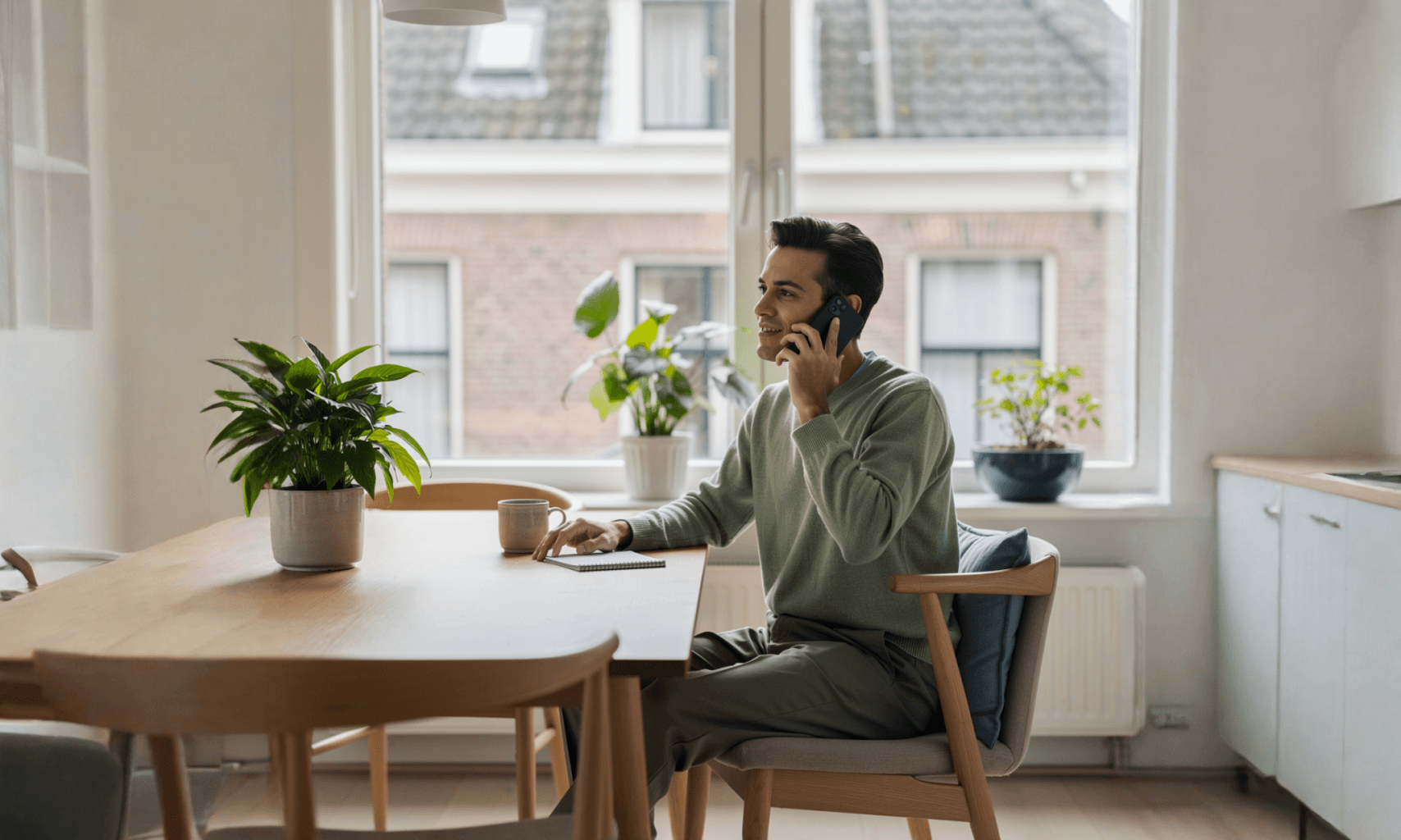 Persoon zit aan een eettafel en voert een telefoongesprek in een lichte woonomgeving