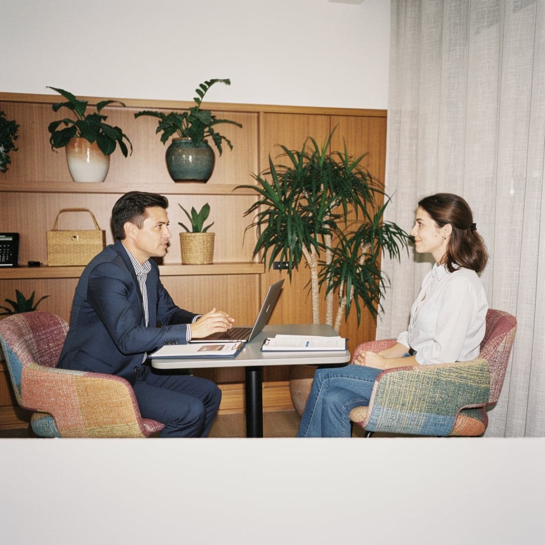 Adviseur en klant zitten tegenover elkaar aan tafel met een laptop en documenten tijdens een gesprek