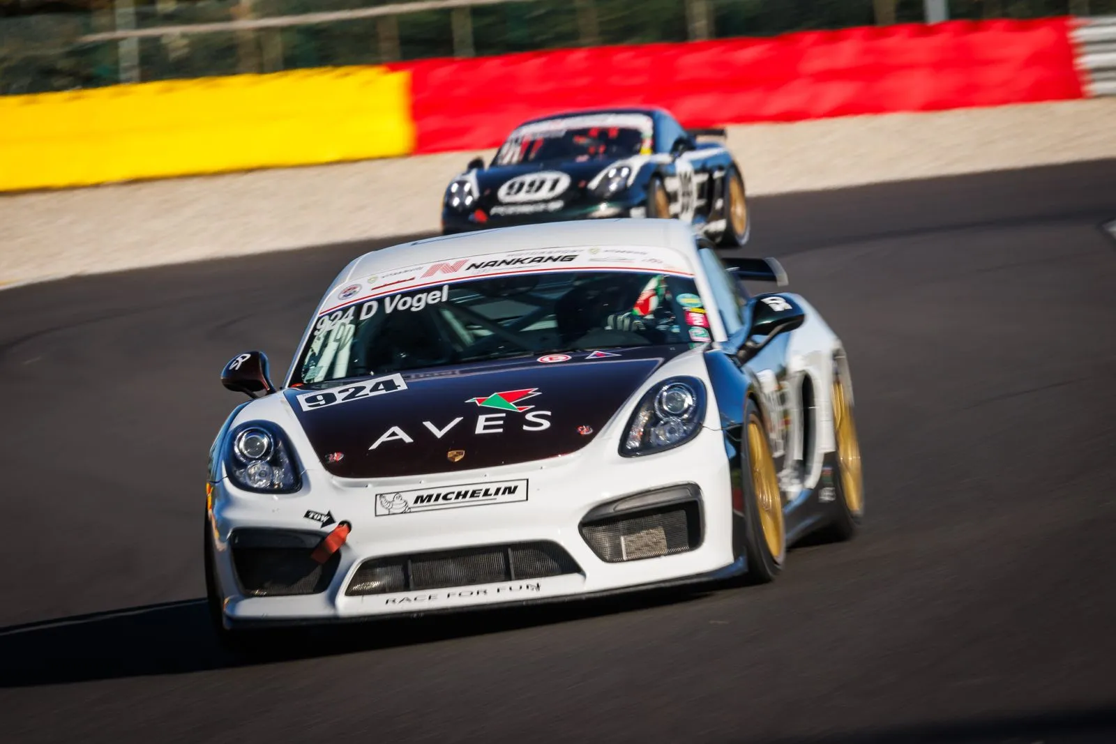 Raceauto rijdt voorop op een bochtig circuit, gevolgd door een andere raceauto